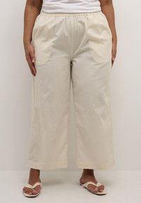 Pantaloni beige a gamba larga realizzati in tessuto leggero, con una vita elastica e tasche laterali, dalla texture liscia e orlo dritto.