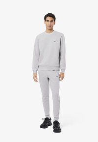 Sudadera gris con logo en el pecho y cuello redondo, combinada con joggers ajustados a juego. Llevada con zapatillas deportivas negras.