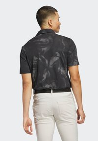 Koszulka polo z krótkim rękawem w kolorze czarnym z teksturowanym wzorem geometrycznym. Posiada klasyczny kołnierzyk i jest zestawiona z jasnobeżowymi spodniami.