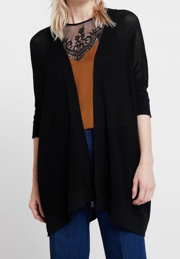 Svart öppenstickad cardigan med trekvartsärmar, med en avslappnad passform och en längre bakre fåll, lagd över en brun topp med spetsdetaljer.
