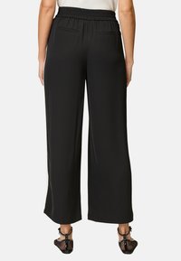Schwarze, weit geschnittene Hose mit einem elastischen Bund. Verfügt über zwei Gesäßtaschen und eine glatte, weiche Textur. Getragen mit Riemchensandalen.