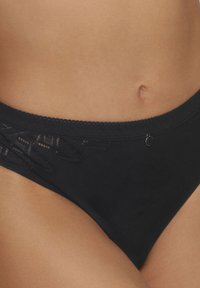 Culottes noires en bikini avec une bordure en dentelle à la taille, présentant une texture douce et un petit accent métallique.