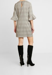 Grå rutad klänning med utsvängda ärmar och detaljer i ryggen, kombinerad med knähöga svarta mockastövlar med sidodragkedjor.