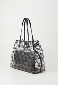 Przezroczysta torba na ramię z czarnym wzorem logo, podwójnymi czarnymi uchwytami i gładką teksturą. Posiada otwarty wierzch oraz kontrastujące, solidne czarne dno.