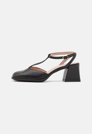Schwarzer Lederschuh für Damen mit T-Riemen, Schnallenverschluss, abgerundeter Spitze und mittelhohem Blockabsatz vor hellem Hintergrund.