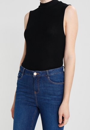Zwarte mouwloze coltrui gecombineerd met blauwe jeans met hoge taille. De stof lijkt glad te zijn met een aansluitende silhouet en minimale details.