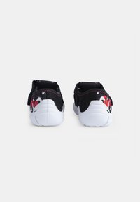 Chaussures en tissu noir avec une semelle blanche, arborant un design graphique coloré à l'arrière et des coutures roses contrastées. Léger et au design simple.
