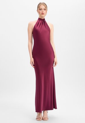 Frau trägt ein ärmelloses, bodenlanges satin gloss burgunderrotes Neckholderkleid und steht vor einem schlichten weißen Hintergrund.