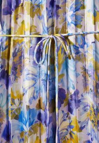 Tissu plissé avec un motif floral jaune, bleu et blanc, noué au centre avec une fine ceinture assortie.
