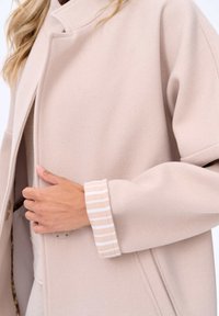 Beige wollen mix jas met een hoge kraag, voorzien van zijzakken en gestreepte accenten op de manchetten. Zachte textuur en oversized pasvorm.