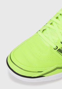 Neon zaļš tenisa apavu modelis ar sintētisku materiālu, teksturētu dizainu, perforācijām gaisa caurlaidībai un melniem akcentiem uz zoles.