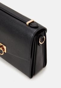 Bolso de mano de cuero negro con un diseño estructurado, acentos de hardware dorado, un asa superior y una vista lateral que muestra un mecanismo de cierre.