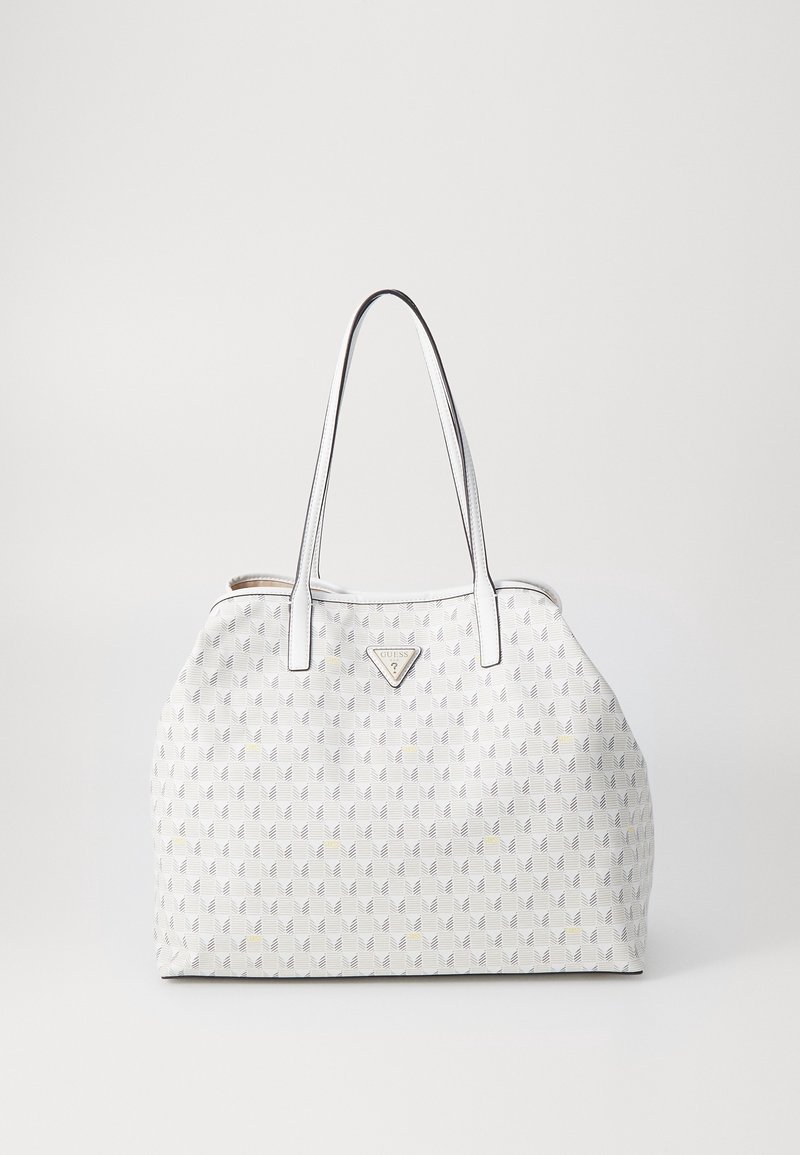 Sac à main blanc avec motif géométrique, double poignée et logo triangulaire Guess sur le devant, sur fond blanc uni.