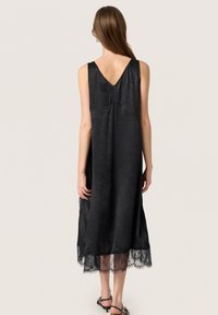 Schwarzes ärmelloses Kleid mit V-Ausschnitt, aus strukturiertem Material und filigranen Spitzenrändern. Locker sitzend für eine entspannte Silhouette.