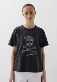 Schwarz Baumwoll-T-Shirt mit einem Frontgrafik eines Totenkopfes mit gekreuzten Knochen und dem Text "Born to be Wild" und "Scalpers Company" in Weiß.