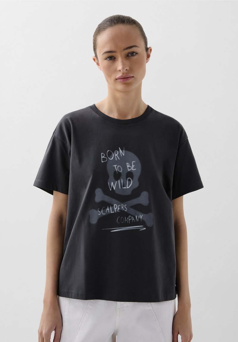 T-shirt en coton noir avec un graphique à l'avant représentant un crâne et des os croisés, accompagné du texte "Né pour être sauvage" et "Scalpers Company" en blanc.