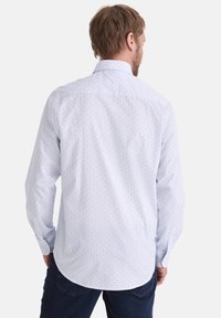 Weißes Hemd mit kleinen navy Punkten, langen Ärmeln und klassischem Kragen. Mit abgerundetem Saum und glatter Baumwollstruktur.