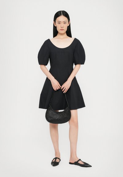 Black short-sleeve dress with a scoop neckline, flared skirt, and textured woven black handbag. Model wears black pointed flats.
