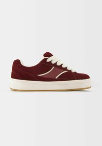 Baskets basses bordeaux avec lacets blancs, semelle blanche et détail d'une bande blanche incurvée sur le côté, présentées de côté extérieur.