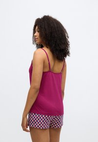 Top justo e sem mangas em algodão magenta escuro, combinado com calções estampados com formas geométricas em azul, roxo e creme.