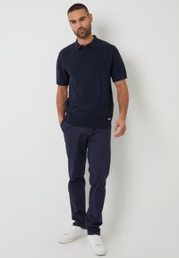 Námořnické polo tričko s texturovaným vzorem, krátkými rukávy a límečkem, v kombinaci s námořnickými kalhotami a bílými teniskami. Diskrétní logo na tričku.