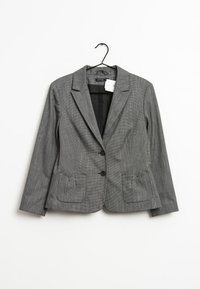 Grå blazer med finestregning, dyb udskæring, to frontlommer og to knapper. Glat stof med en subtil struktur. Hænger fra en sort krog.