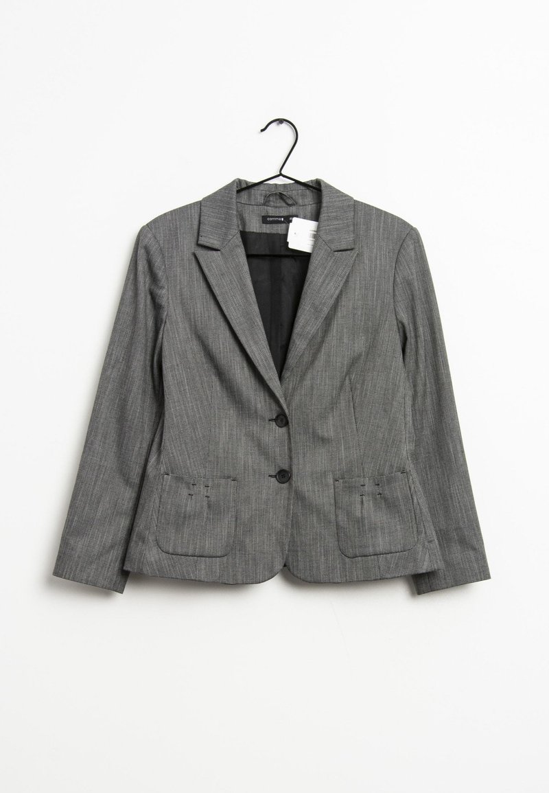 Grå blazer med finestregning, dyb udskæring, to frontlommer og to knapper. Glat stof med en subtil struktur. Hænger fra en sort krog.