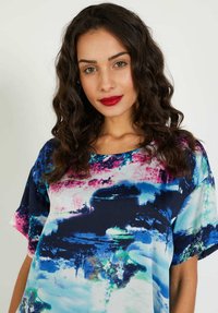 Blusa de manga corta en tejido ligero con un patrón abstracto en azul, rosa y blanco, con un escote amplio y un corte relajado.