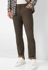 Bruine, op maat gemaakte broek van gestructureerde stof, met zijzakken en een opgerolde zoom. Gecombineerd met witte sneakers voor contrast.