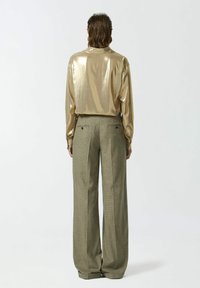 Sjajna zlatna košulja dugih rukava s visokim ovratnikom uparen s širokim, svijetlozelenim kariranim hlačama s stražnjim džepovima.