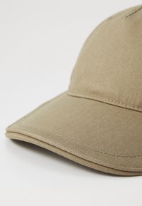 Cappellino da baseball color khaki realizzato in tessuto testurizzato, caratterizzato da una visiera curvata, dettagli cuciti e un design a corona strutturata.