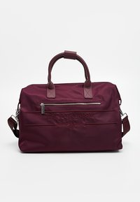 Tummanpunainen duffel-laukku kestävästä kankaasta, jossa on vetoketjullinen etutasku, kaksinkertaiset kahvat ja irrotettava olkahihna. Painettu logovetoketju.