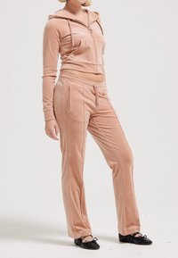 Tuta in velluto di un delicato rosa pallido, composto da una felpa cropped con zip e pantaloni con coulisse, dotato di tasche frontali e una superficie morbida e liscia.
