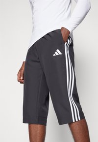 Dunkelgraue Sportshorts aus atmungsaktivem Material, mit weißen drei Streifen Akzenten und einem Adidas-Logo auf dem linken Bein.