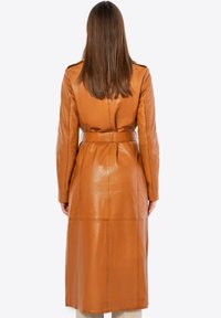 Trench coat de cuero marrón con mangas largas, cintura ceñida con cinturón, detalles en las costuras y una textura suave y brillante. Apariencia de longitud hasta la mitad de la pantorrilla.