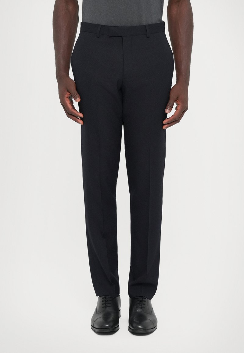 Hose aus dunkelblauem Stoff mit taillierter Passform, flachem Bund und zwei seitlichen Taschen, kombiniert mit schwarzen Dressschuhen.