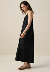 Robe maxi sans manches noire avec une coupe décontractée, dotée d'une texture douce et lisse. Associée à des sandales à talons imprimé léopard.
