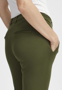 Olive zelene prilegače hlače z gladko teksturo, pasom, dvema zadnjima žepoma in stranskim žepom za roke, zasnovane za prilagojen kroj.