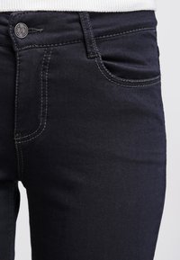 Mørke denimjeans med en glatt tekstur, som har en klassisk fem-lommers design, matchende sømmer og en metallknapp-lukking i midjen.