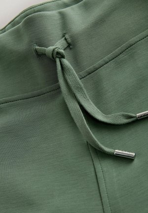Détail de cordon de serrage vert avec agrafes métalliques et ceinture lisse, présentant une texture de tissu douce et légère ainsi qu'un design simple.