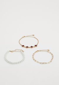 Three bracelets: gold chain with red gemstones, gold chain with links, and white pearl beads with gold clasps on white background.