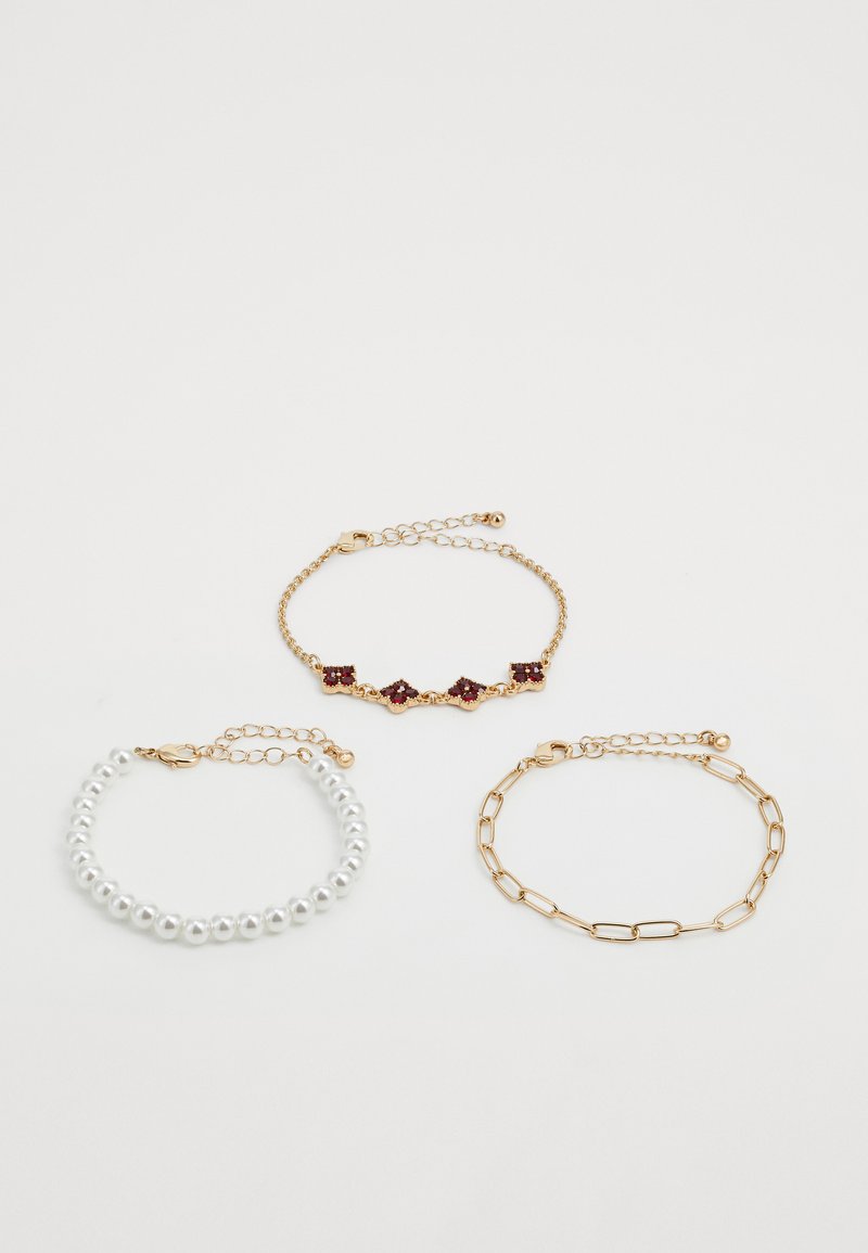 Three bracelets: gold chain with red gemstones, gold chain with links, and white pearl beads with gold clasps on white background.
