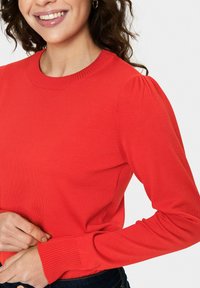 Rdeč pleten pulover z rebrastim okroglim ovratnikom in napihnjenimi dolgimi rokavi, z teksturirano tkanino in prilegajočimi manšeti.