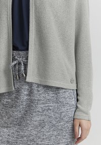 Ljust grå stickad cardigan med en l�ös passform, som har ett mönster med textur. Kombinerad med en grå kjol med dragsko, accentuerad med silverdetaljer.