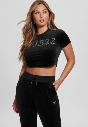 T-shirt cropped in velluto nero con "GUESS" in strass, abbinato a pantaloni in velluto nero coordinati con vita regolabile e dettaglio del logo.