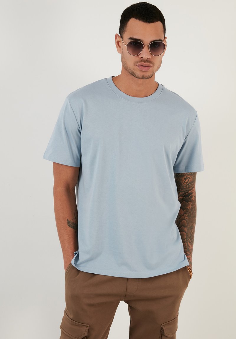 Tricou scurt cu mânecă scurtă de culoare albastru deschis, realizat dintr-un material moale, cu guler rotund, croi lejer și detalii de cusătură subtile.