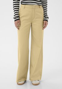 Pantalon beige à jambes larges en tissu doux, doté d'une taille classique et de peu de matériel. Porté avec un top rayé noir et blanc.