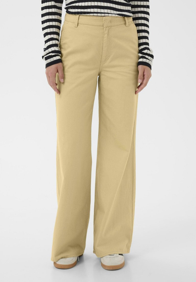 Pantalon beige à jambes larges en tissu doux, doté d'une taille classique et de peu de matériel. Porté avec un top rayé noir et blanc.