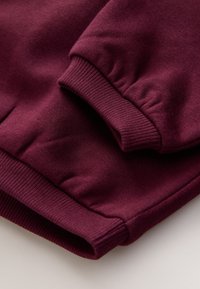 Primer plano de una manga doblada de sudadera burdeos que muestra el puño acanalado y la textura suave de la tela.