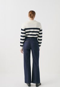 Raidallinen neule vaaleassa kermanvärissä ja tummansinisessä, leveälahkeiset tummat denimit, ja mustat kengät. Sisältää ribattu kaulus ja takataskut farkuissa.